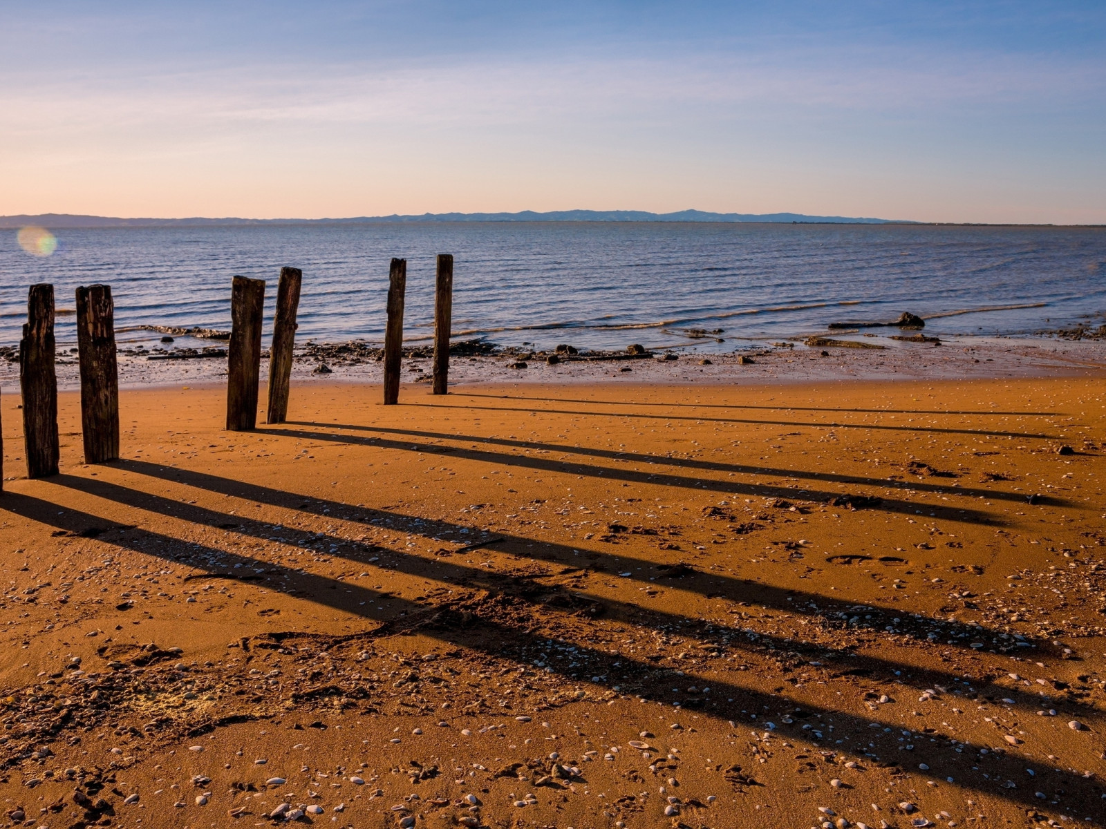 Sombras de pilares de madera sobre playa arenosa